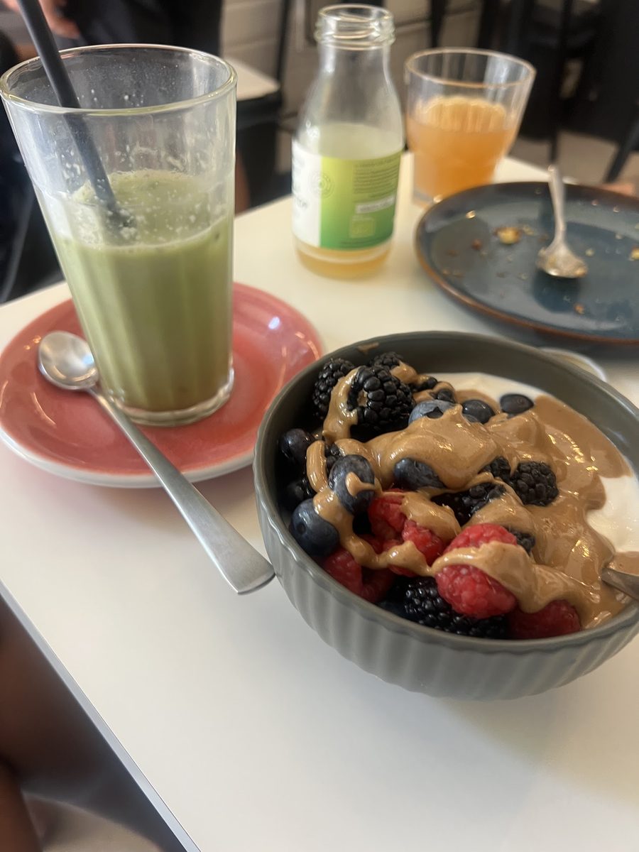 Yogurt bowl con frutti di bosco e burro di arachidi accanto a un matcha latte